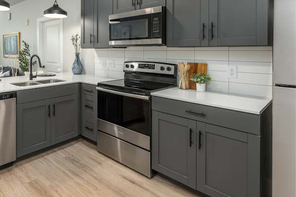 A modern kitchen with dark grey cabinets and stainless steel appliances.